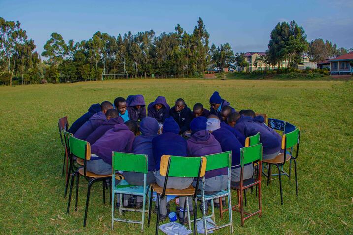 Group of people sitting in chairs in grass huddled into a circle; Shamiri Institute, Inc